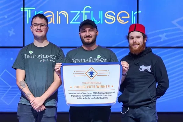 Shiverbug Studios' three co-founders on stage at Tranzfuser 2025, holding an oversized Public Vote Winner certificate between them, beneath a large lit Tranzfuser sign.