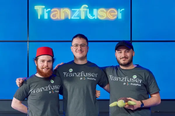 Shiverbug Studios' three co-founders on stage at Tranzfuser 2025 in Tranzfuser at ProtoPlay t-shirts, beneath a neon Tranzfuser sign